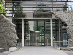 Moderne Glasfassade des Gebäudes der Max-Planck-Gesellschaft, flankiert von Steinskulpturen.