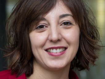 Guadalupe Moreno Das Porträt eines vermutlich weiblichen Exemplars der Gattung Homo sapiens intellectualis nimmt das Foto fast vollständig ein. Es hat schulterlanges, dichtes schwarzes Haar, das zur rechten Seite teils eine Augenbraue verdeckt. Die dunklen Augen schauen freundlich, zeigen jedoch Anzeichen einer gewissen Übermüdung. Das tut dem herzlich-empathischen Eindruck, der sich dem Betrachter vermittelt, keinen Abbruch. Der Mund ist halb zu einem verschmitzten Lächeln geöffnet, saubere, gesunde weiße Zähne deuten auf intensive Pflege hin. Die rote Bluse mit Kragen verfügt über einen weiten Ausschnitt, der genügend Raum lässt für die goldene Kette, an der als Symbol ein Kreuz hängt, möglicherweise ein Hinweis auf die religiöse Grundgestimmtheit des Individuums. Alles in allem drückt das Antlitz eine nicht mehr oft anzutreffende Weltzugewandtheit aus – offenherzige Sympathie kommt zum Vorschein.