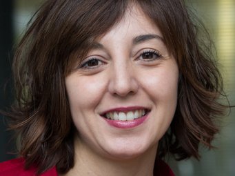 Guadalupe Moreno The portrait of what is presumably a female specimen of the species Homo sapiens intellectualis takes up almost the entire photo. She has shoulder-length, thick black hair, which partially covers one eyebrow on the right side. Her dark eyes look friendly, but show signs of fatigue. This does not detract from the warm and empathetic impression she conveys to the viewer. The mouth is half open in a mischievous smile, and clean, healthy white teeth indicate intensive care. The red blouse with a collar has a wide neckline that leaves enough room for the golden chain with a cross pendant, possibly an indication of the individual's religious disposition. All in all, the face expresses a worldliness that is no longer often found – open-hearted sympathy shines through.