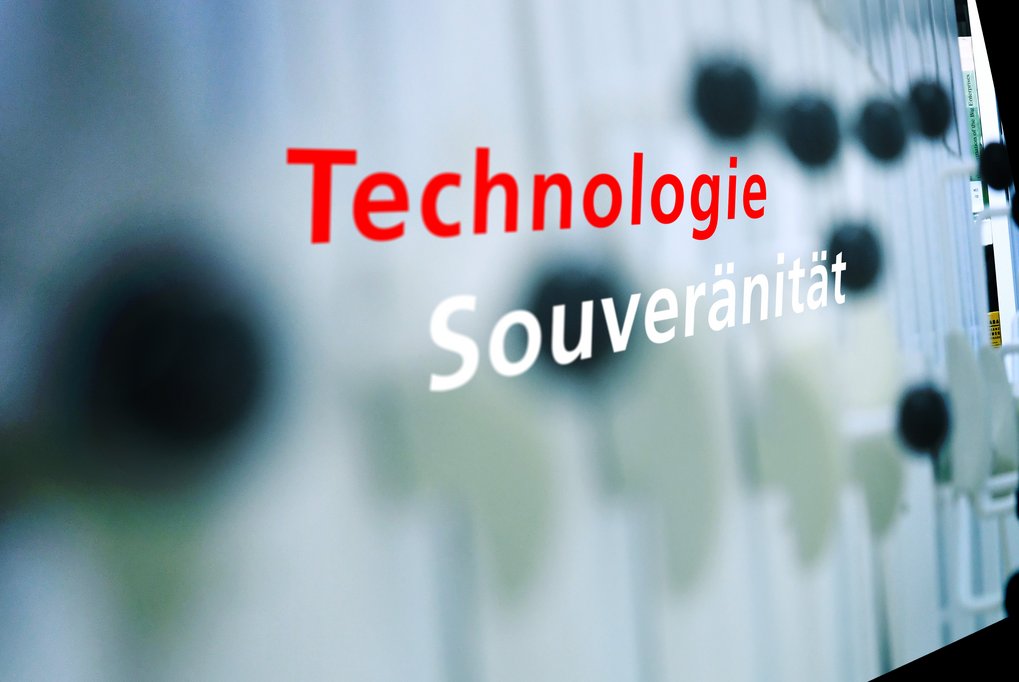 Illustrationsbild: Im Vordergrund die Stichworte „Technologische Souveränität“, im Hintergrund verschwommene Griffe eines beweglichen Regalsystems für Bibliotheken.