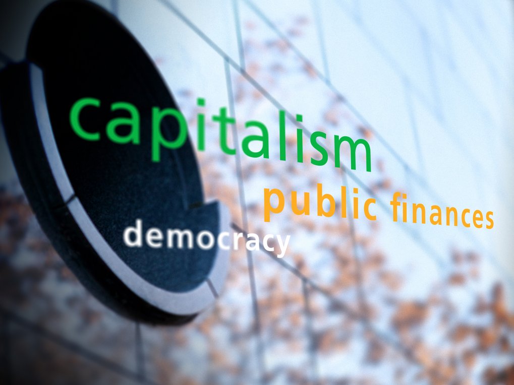 Text on a wall featuring the words "capitalism," "public finances," and "democracy," with a modern design and abstract background.