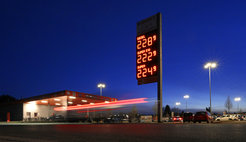 Tankstelle bei Nacht mit beleuchteter Preisanzeige für Kraftstoffe, darunter Diesel, Super E10 und Super, umgeben von parkenden Autos.