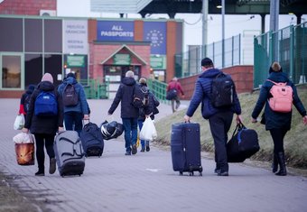 Infolge des russischen Angriffskrieges gegen die Ukraine kommen gegenwärtig immer mehr Flüchtende in Deutschland an. Um sie zu unterstützen, wird versucht, die Fluchtrouten in alle Mitgliedsstaaten der Europäischen Union sicherer und auch weniger kostspielig zu gestalten: Die EU-Grenzen sind für ukrainische Flüchtende offen, nach einem Beschluss vom 4. März 2022 wird ihnen ein bis zu drei Jahre währender Schutzstatus zugesichert, und in vielen Ländern dürfen Züge zum Transport kostenlos genutzt werden. Trotz dieser Versuche, die Gefahren einer Flucht zu mindern, bleibt sie gefährlich und auch teuer. Eine Gruppe von Menschen mit Koffern und Taschen bewegt sich auf einen Grenzübergang zu, der für alle Pässe offen ist, bei kühlem Wetter.