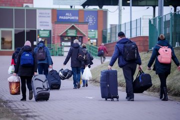 Eine Gruppe von Menschen mit Koffern und Taschen bewegt sich auf einen Grenzübergang zu, der für alle Pässe offen ist, bei kühlem Wetter.