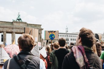 Eine Gruppe von Demonstranten versammelt sich mit Umweltschutz-Plakaten vor dem Brandenburger Tor. Im Hintergrund ist eine Skulptur zu sehen.