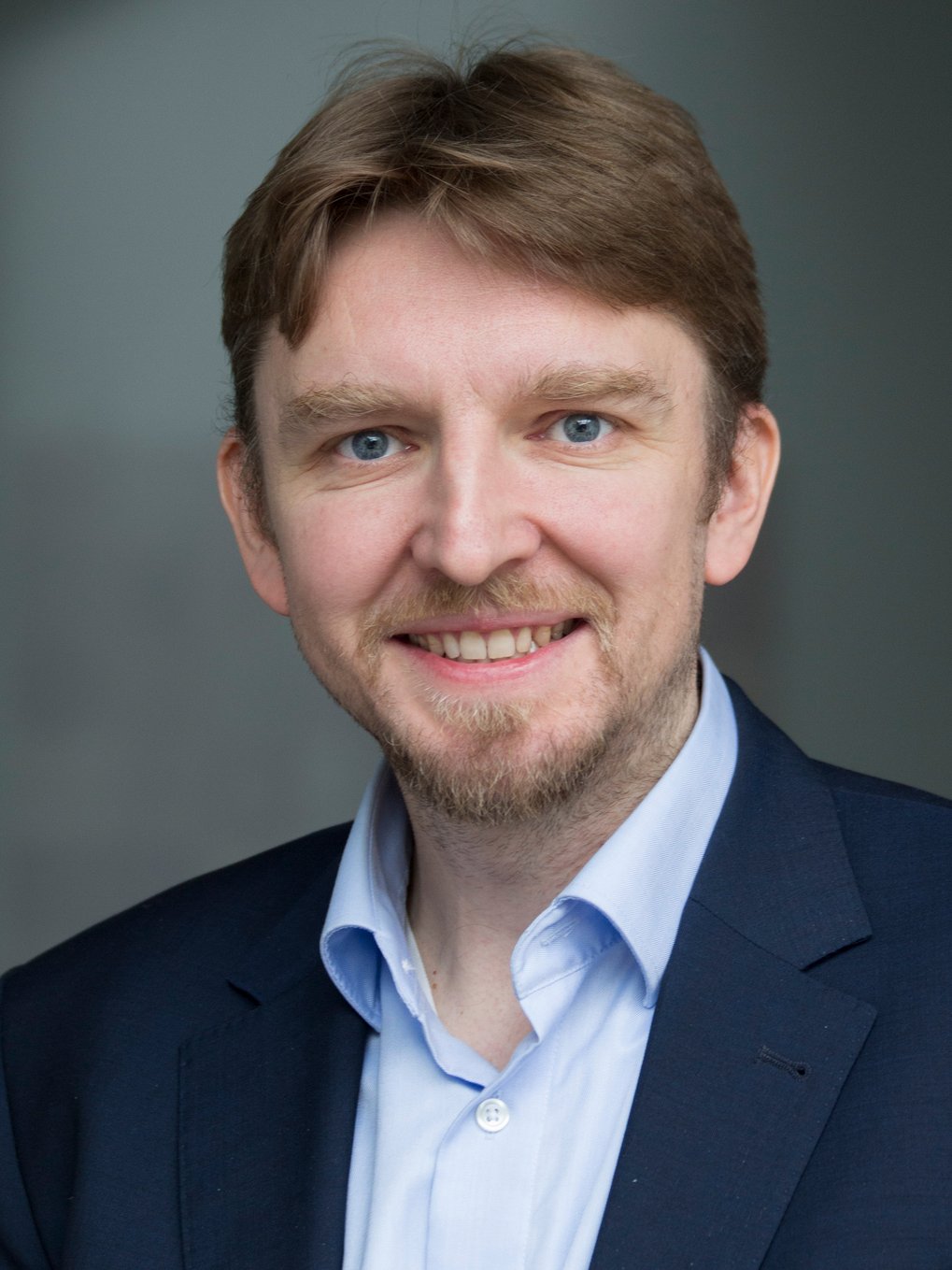 A golden statue of Lady Justice, holding scales in her right hand and a sword in her left, stands in a modern urban space surrounded by tall buildings and a stone wall.