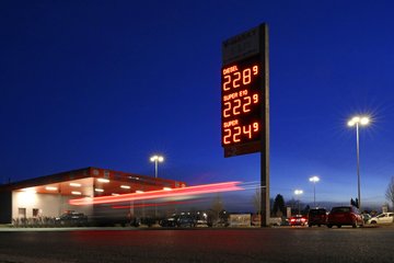 Tankstelle bei Nacht mit beleuchteter Preisanzeige für Kraftstoffe, darunter Diesel, Super E10 und Super, umgeben von parkenden Autos