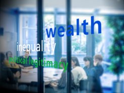 A group of people sits in a meeting room, visible through a glass wall displaying the words "wealth," "inequality," and "political legitimacy."