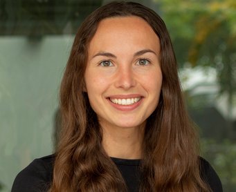 Hannah Pool Junges, vermutlich weibliches Exemplar der Gattung Homo sapiens intellectualis. Es trägt das mittellange dunkelbraune Haar offen zur Mitte gescheitelt und lächelt offen-freundlich empathisch dem Betrachter zu. Der Hintergrund ist nicht definierbar.