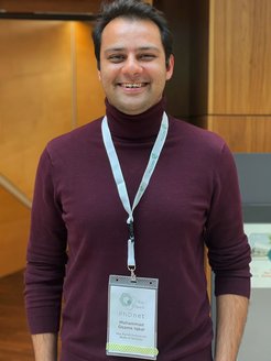 A person in a burgundy sweater, wearing a lanyard with a badge labeled "PhDnet" from Max Planck Institute for the Study of Societies.