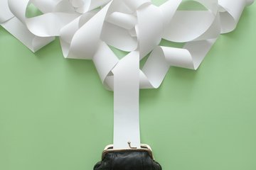 Eine schwarze Geldbörse auf einem grünen Hintergrund, aus der sich lange, weiße Papierstreifen erstrecken und den oberen Bereich des Bildes füllen.