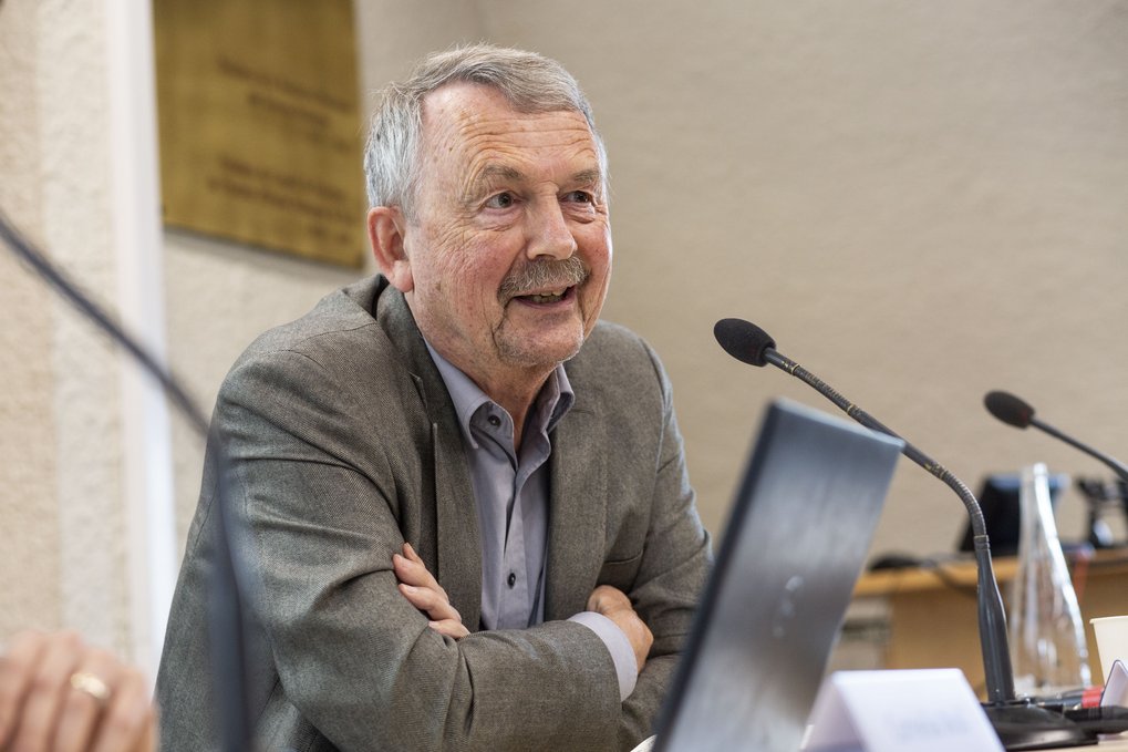 Ein Mann sitzt an einem Tisch mit einem Computer und einem Mikrofon, lächelt und unterhält sich angeregt.