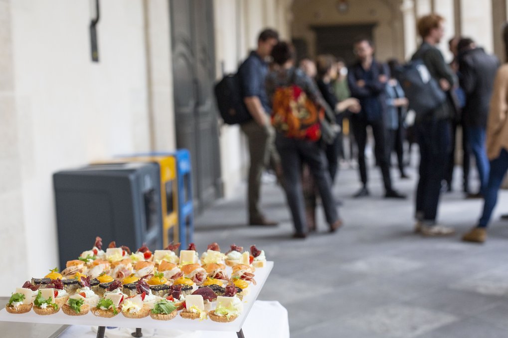 Ein Tisch mit einer Auswahl an Vorspeisen im Vordergrund, im Hintergrund eine Gruppe von Menschen, die sich unterhalten.