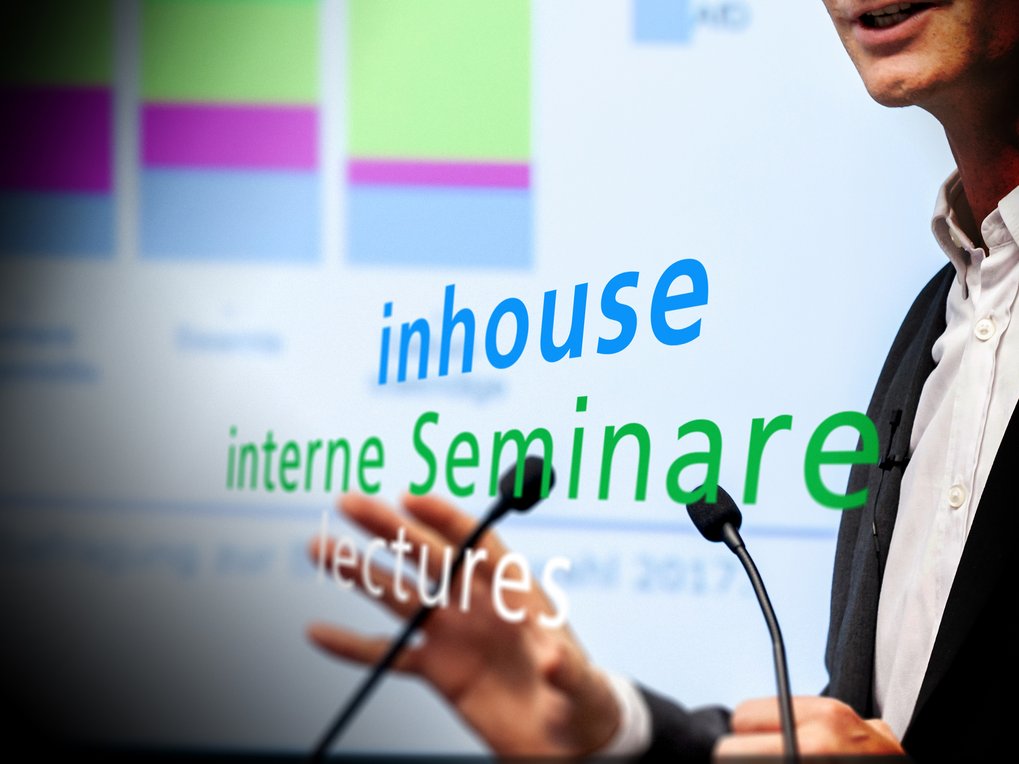 Ein Redner, der vor einer Leinwand steht, auf der Texte zu den Themen „inhouse“, „interne Seminare“ und „Vorträge“ angezeigt werden.