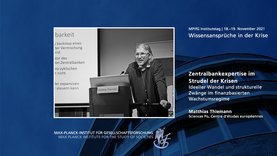 Das Bild zeigt den Redner Matthias Thiemann bei einem Vortrag auf einer Konferenz mit dem Titel „Wissensansprüche in der Krise”. Der Inhalt befasst sich mit der Expertise von Zentralbanken in Krisenzeiten und enthält Text in deutscher Sprache.
