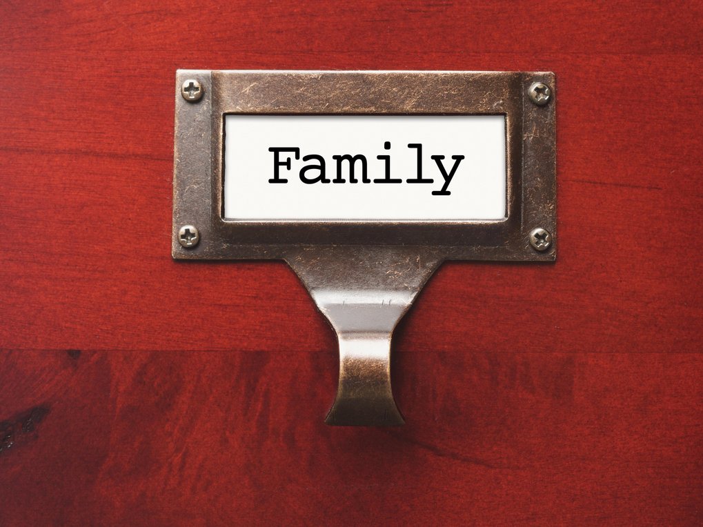 Ein rechteckiger Metallrahmen, befestigt auf einer roten Holzoberfläche, zeigt das Wort "Family" in schwarzer Schrift.