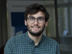Auf dem Foto ist ein vermutlich junges männliches Exemplar der Gattung Homo sapiens intellectualis zu erkennen. Es trägt auf der Nase eine Brille, die der verfeinerten optischen Wahrnehmung zweckdienlich ist. Das Individuum hat den Mund zu einem als optimistischem Lächeln interpretierbaren Gestus geöffnet. Nicht unerwähnt darf bleiben, dass das Individuum einen bereits ausgeprägten Bartwuchs aufweist, das auf einen Rasierverzicht von nicht weniger als einer zweiwöchigen Dauer hindeutet.
