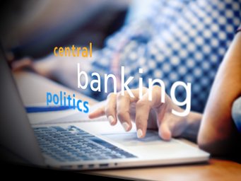 Close-up of a hand typing on a laptop keyboard; words "central," "banking," and "politics" are layered over the image, suggesting themes of finance and governance.