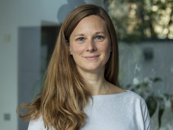 Das Foto zeigt die Soziologin Isabell Stamm, die am MPIfG über mehrere Jahre eine Forschungsgruppe geleitet hat. Die junge, zaghaft lächelnde Frau hat langes blondes Haar, das sie teilweise in gelungener Manier nach vorn gen Brust geschwungen hat. Sie trägt einen hellblauen Pullover, der farblich ganz trefflich mit ihren blauen Augen abgestimmt ist.