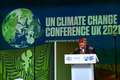 Bühne mit UN-Klimakonferenz 2021 Banner, Rednerpult und tropischen Pflanzen im Vordergrund. Ein Mikrofon steht links neben dem Rednerpult.