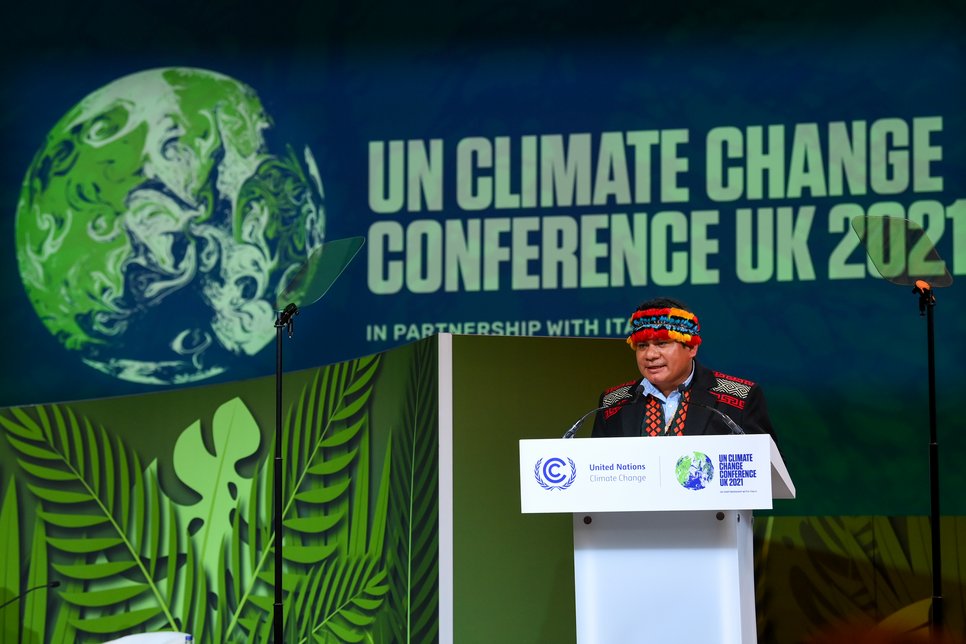 Bühne mit UN-Klimakonferenz 2021 Banner, Rednerpult und tropischen Pflanzen im Vordergrund. Ein Mikrofon steht links neben dem Rednerpult.
