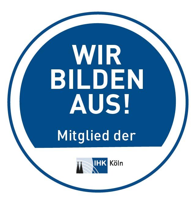 Rundes blaues Emblem mit weißem Schriftzug "Wir bilden aus! Mitglied der IHK Köln" und IHK-Logo am unteren Rand.