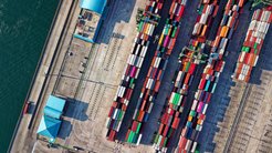 Aerial view of a port terminal with numerous colorful shipping containers aligned in rows, adjacent to the waterfront, and nearby port facilities.