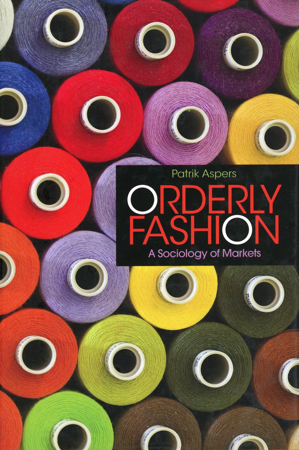 Verschiedene farbige Garnspulen sind um das Buch "Orderly Fashion: A Sociology of Markets" von Patrik Aspers angeordnet, das in Schwarz und Rot gestaltet ist.
