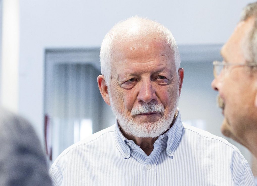 An elderly man with a beard is engaged in conversation with another man, both appearing to be in a professional or social setting.