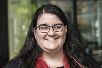 Eine Person mit langen, dunklen Haaren und roten Spitzen steht vor einem unscharfen Hintergrund, der auf eine Umgebung im Freien hinweisen könnte. Ein Foto zeigt Danielle Pullan, die im August 2025 Assistenzprofessorin in den USA wird.