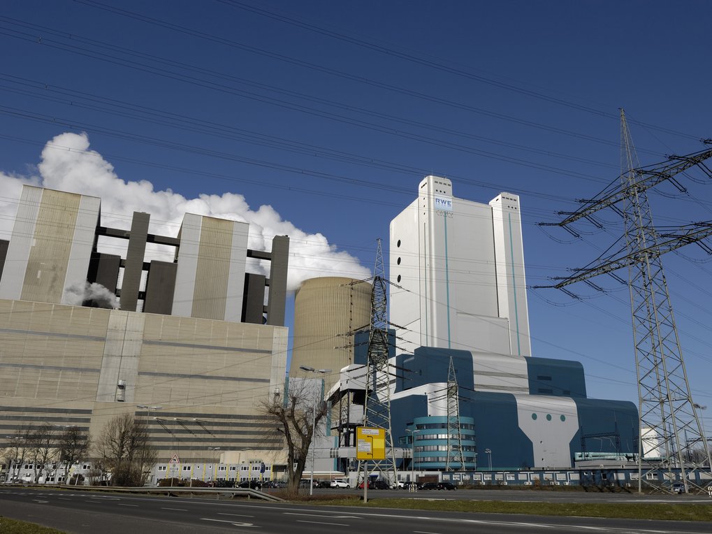 Braunkohlekraftwerk, blauer Himmel, Strommast mit Leitungen davor, Straße im Vordergrund. Credit: istock/acilo