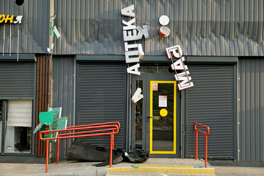 Eine geschlossene gelbe Tür mit roten Geländern, umgeben von heruntergefallenen Schildern an einer beschädigten Gebäudefassade in der Ukraine