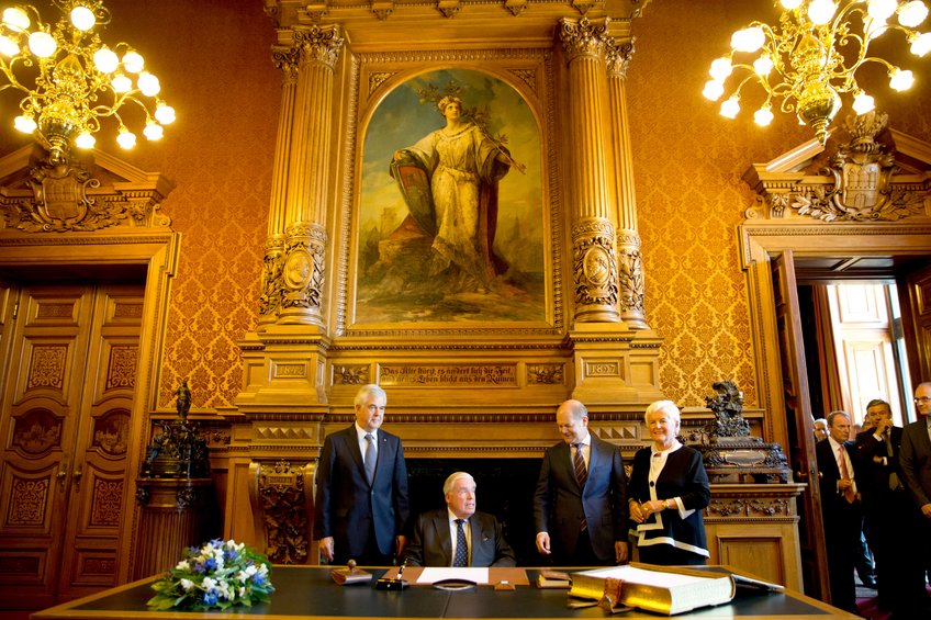 Hamburg-based logistics entrepreneur and investor Klaus-Michael Kühne (second from left) has been among Germany's wealthiest individuals for many decades, with an estimated fortune of 36 billion US dollars. He is the third generation of the Kühne family to head Kühne+Nagel, under his leadership now one of the largest logistics companies in the world. On July 1, 2015, he signed the city's Golden Book at Hamburg City Hall alongside the then mayor of Hamburg and later German chancellor Olaf Scholz. The occasion was Kühne+Nagel's 125th anniversary. Klaus-Michael Kühne at the desk next to the then mayor of Hamburg and later Chancellor Olaf Scholz in a room with golden wallpaper and chandeliers.