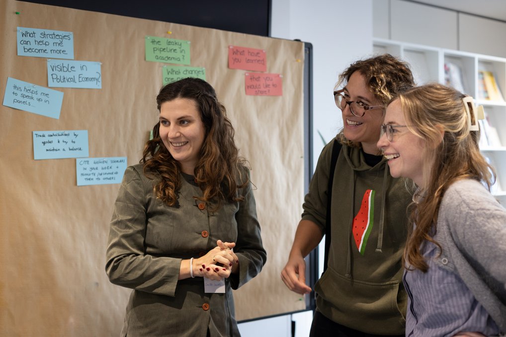 Three participants talking and smiling in front of a poster wall
