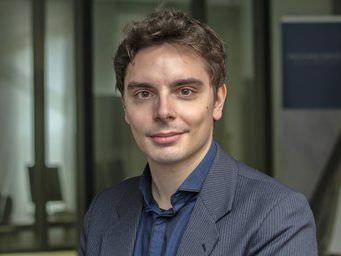 Person in gestreiftem Anzug, Hintergrund mit Glaswand und Plakat.