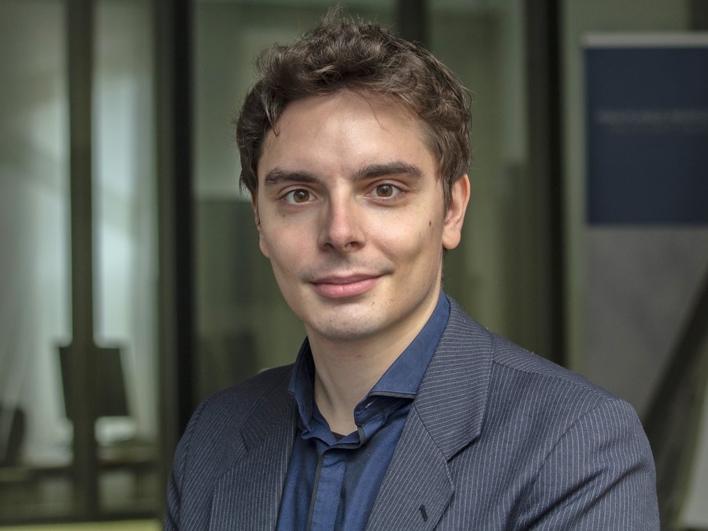 Person in a striped suit, background with glass wall and poster.
