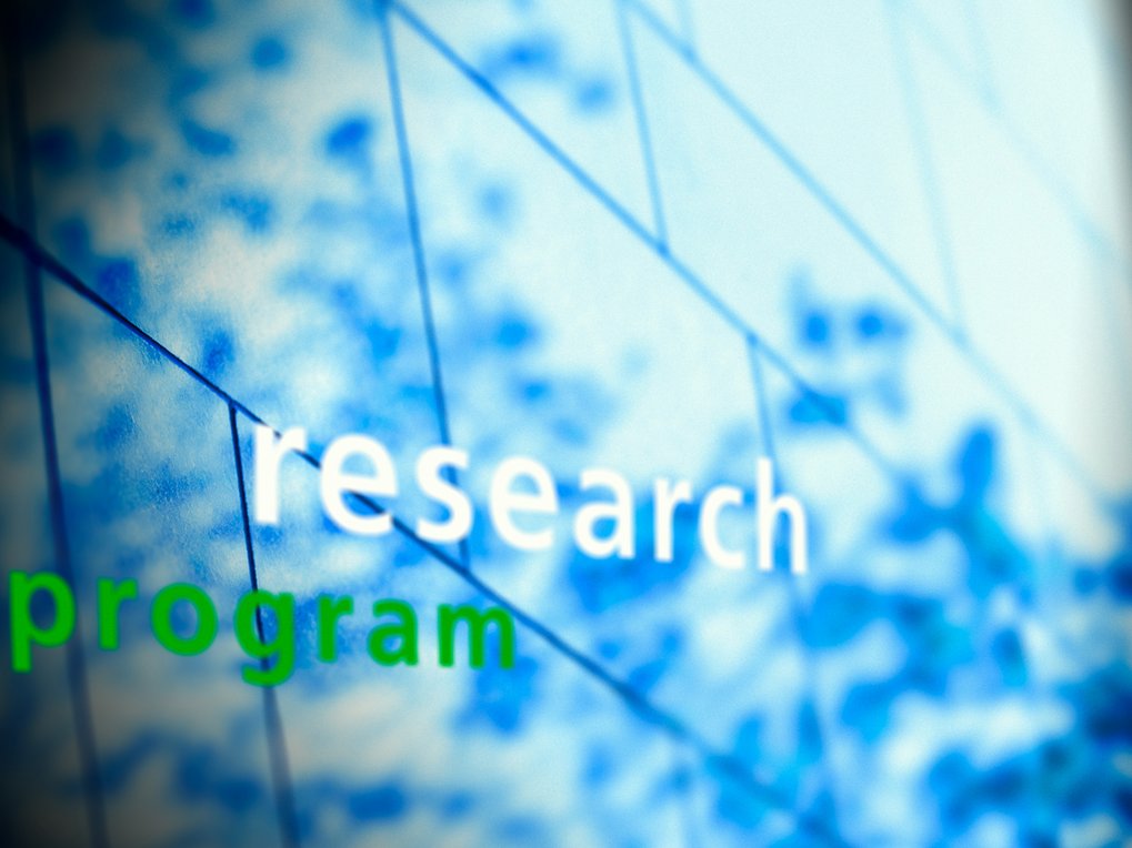 The image displays the words "research program" in sharp focus against a blurred blue background, possibly representing innovation.