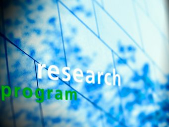 The image displays the words "research program" in sharp focus against a blurred blue background, possibly representing innovation.