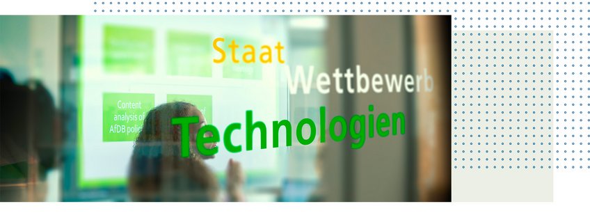 Technologie und Staatlichkeit Auf einer Glasfläche sind die Worte „Staat, Wettbewerb, Technologien“ zu sehen, hinter denen digitale Inhalte angezeigt werden.