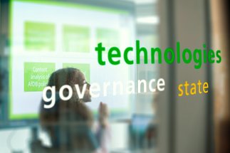 Words like "technologies," "governance," and "state" appear on glass, reflecting a screen's content.