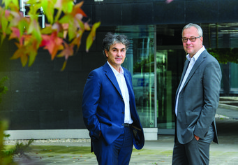 The MPIfG directors in the backyard of the MPIfG office building Two men in business suits stand near a modern building entrance.