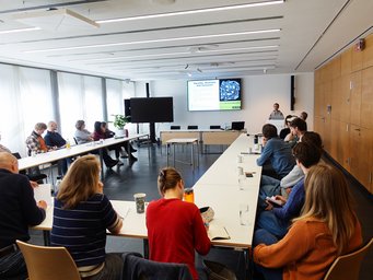 In einem hellen Konferenzraum verfolgen mehrere Personen einen Vortrag über Gleichheit, Vielfalt und Inklusion auf einem Bildschirm.