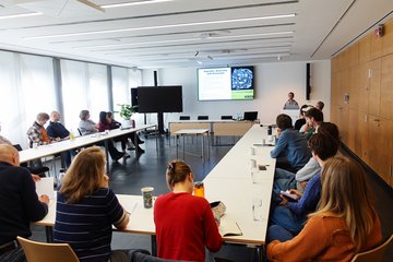In a brightly lit conference room, several people are watching a presentation on equality, diversity, and inclusion on a screen.