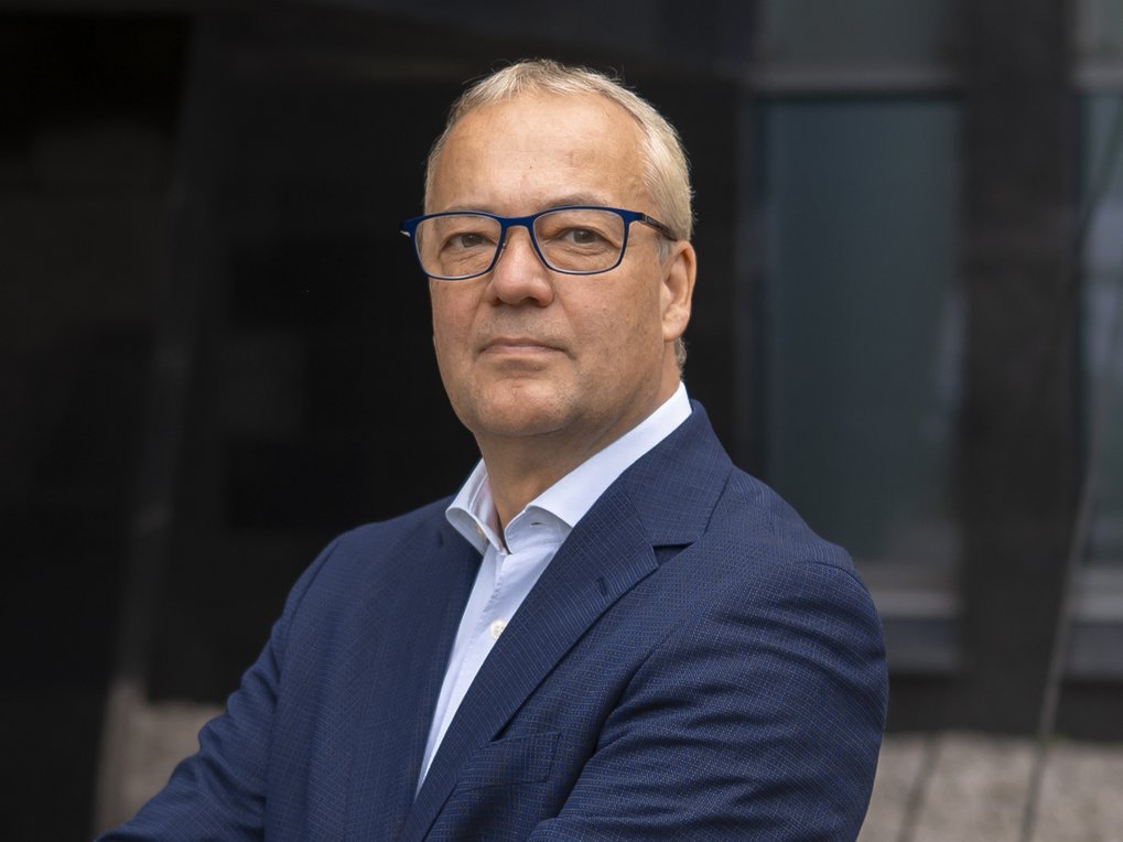 Mann mit Brille im Anzug mit offenem Hemd vor dunkliem Hintergrund stellt sich dem Fotografen.
