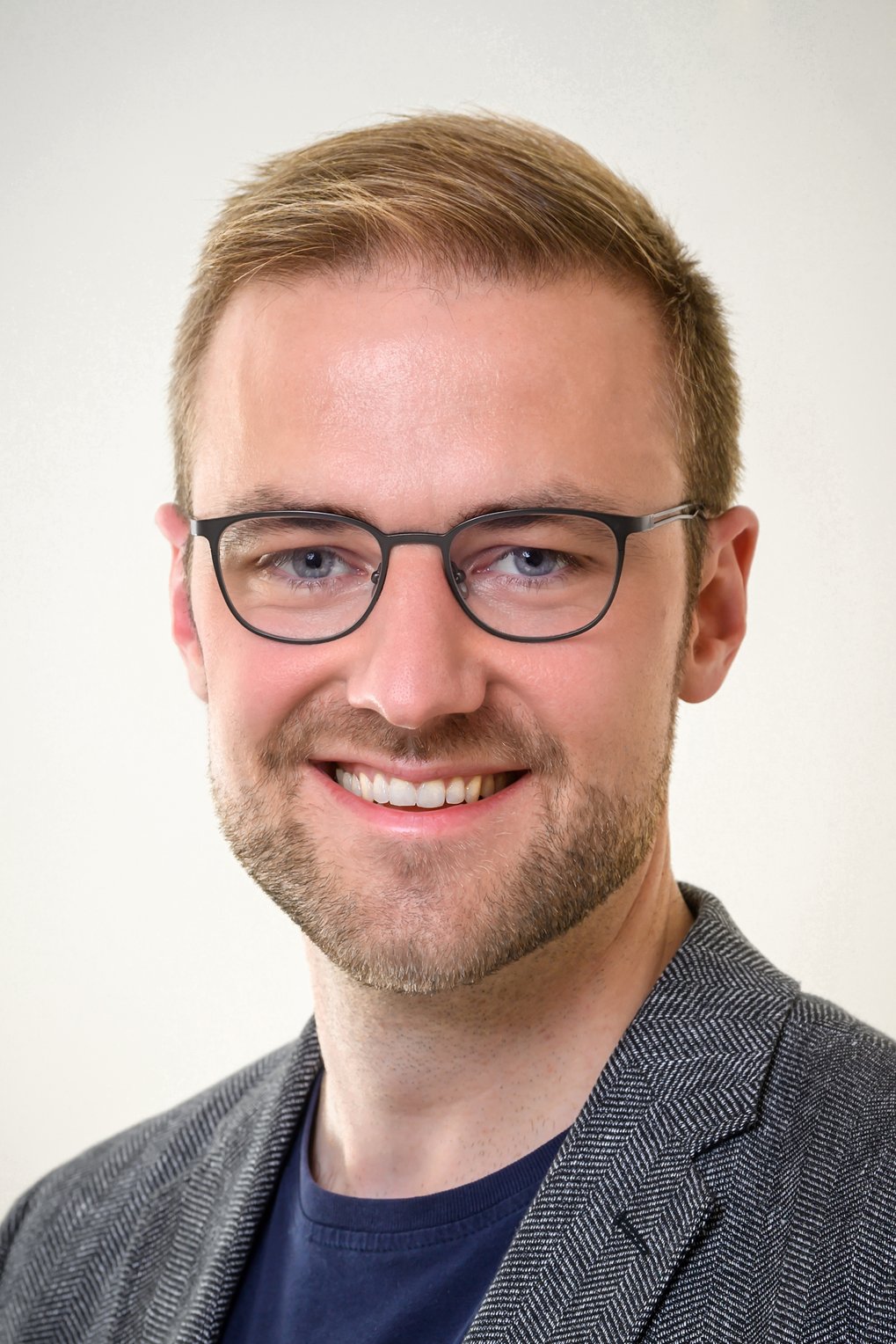 Ein gesundes, bebrilltes, kurzhaariges, leicht bebartes Exemplar der Gattung Homo sapiens intellectualis mittleren Alters grinst friedlich-fröhlich dem Betrachter entgegen. 