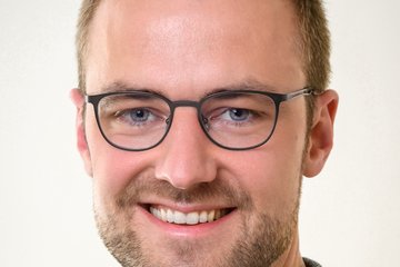 A healthy, bespectacled, short-haired, slightly bearded specimen of the species Homo sapiens intellectualis, of middle age, grins peacefully and cheerfully at the viewer.
