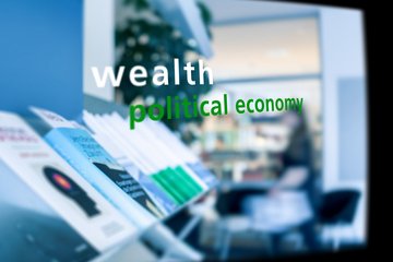 Bücherreihe zu politischen und wirtschaftlichen Themen in einem Regal, im Hintergrund unscharfe Sitzgelegenheiten und Personen in einem Innenraum