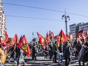 Demonstration mit vielen roten Fahnen und zahlreichen Teilnehmenden in einer Stadt.
