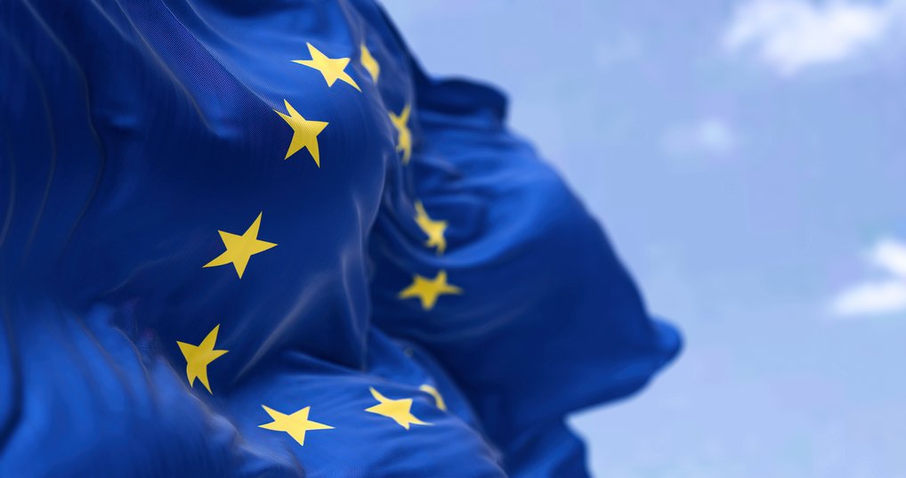 Nahaufnahme der wehenden Europaflagge mit zwölf gelben Sternen auf blauem Grund vor blauem Himmel.