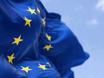 Nahaufnahme der wehenden Europaflagge mit zwölf gelben Sternen auf blauem Grund vor blauem Himmel.